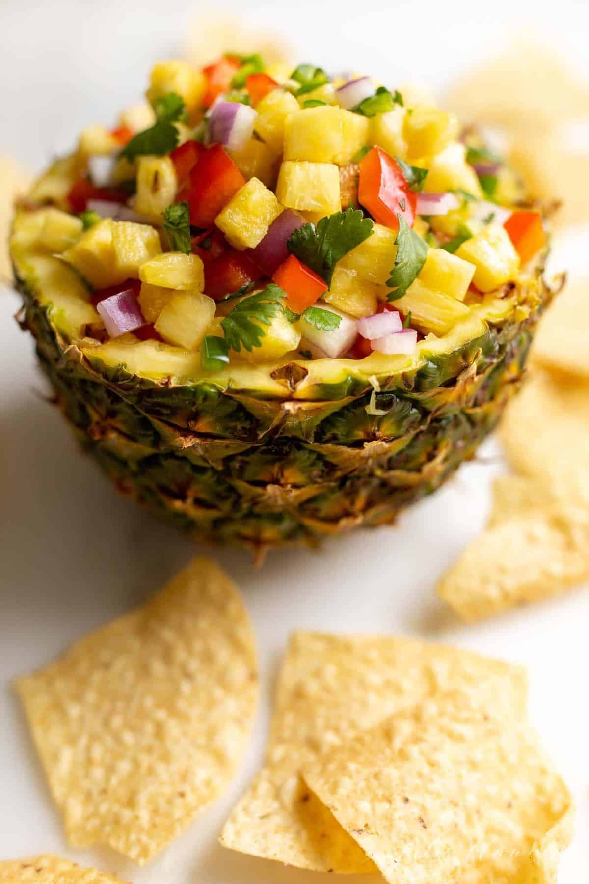 A fresh bowl made from a cut pineapple, filled with pineapple salsa, tortilla chips surrounding.