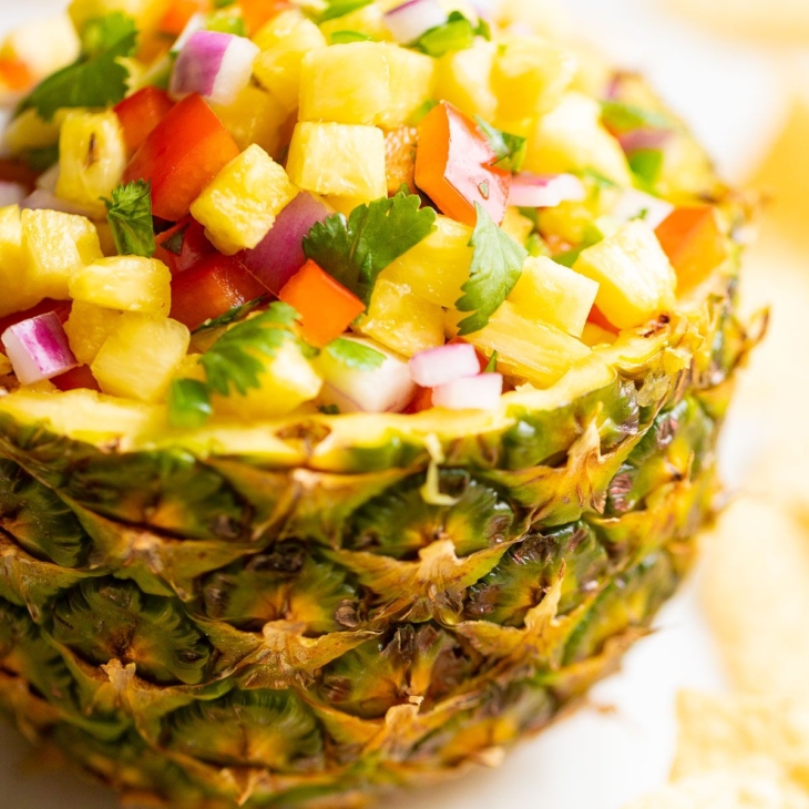 Pineapple salsa inside a pineapple bowl, on a white countertop. surrounded by tortilla chips.