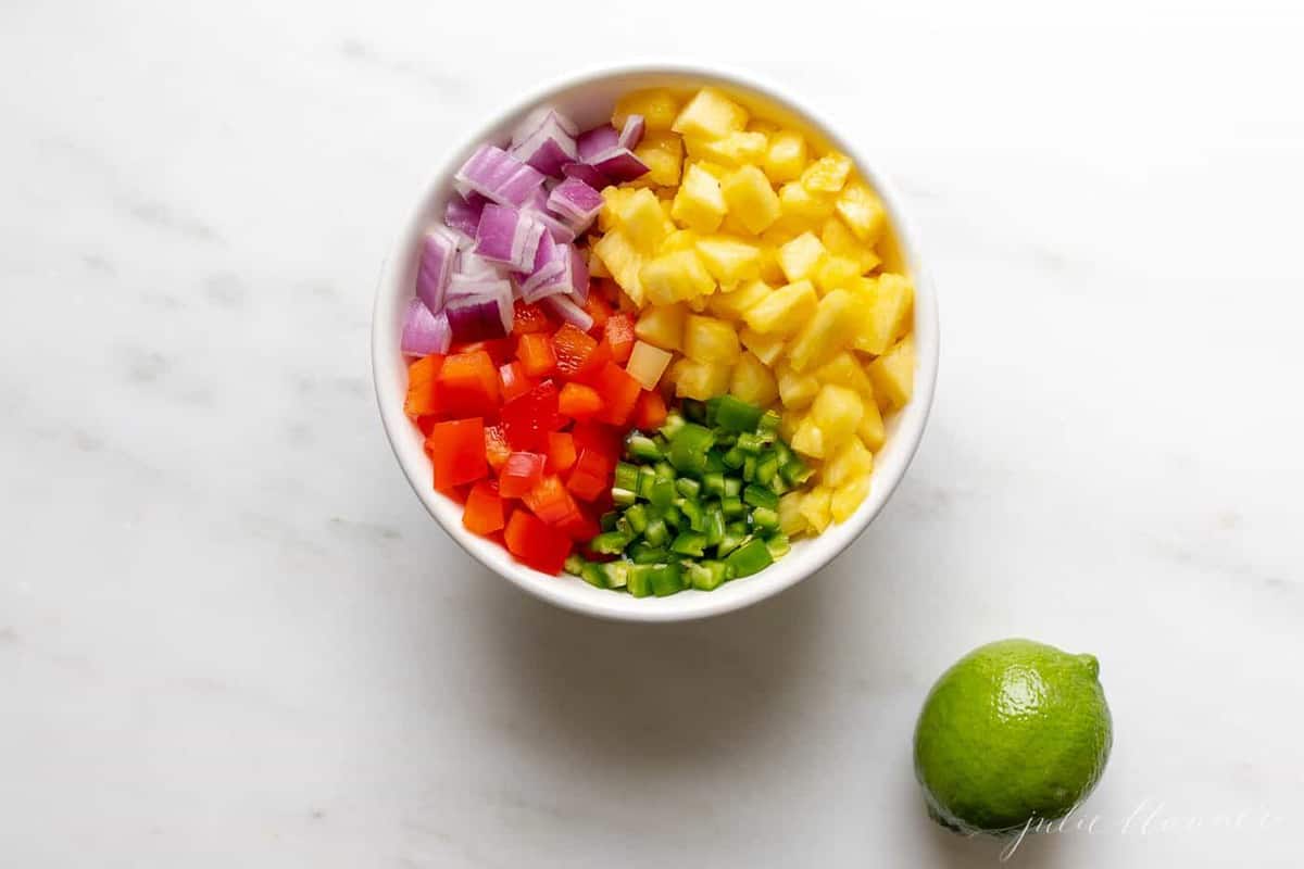 Pineapple salsa ingredients in a white bowl, with a lime to the side. 