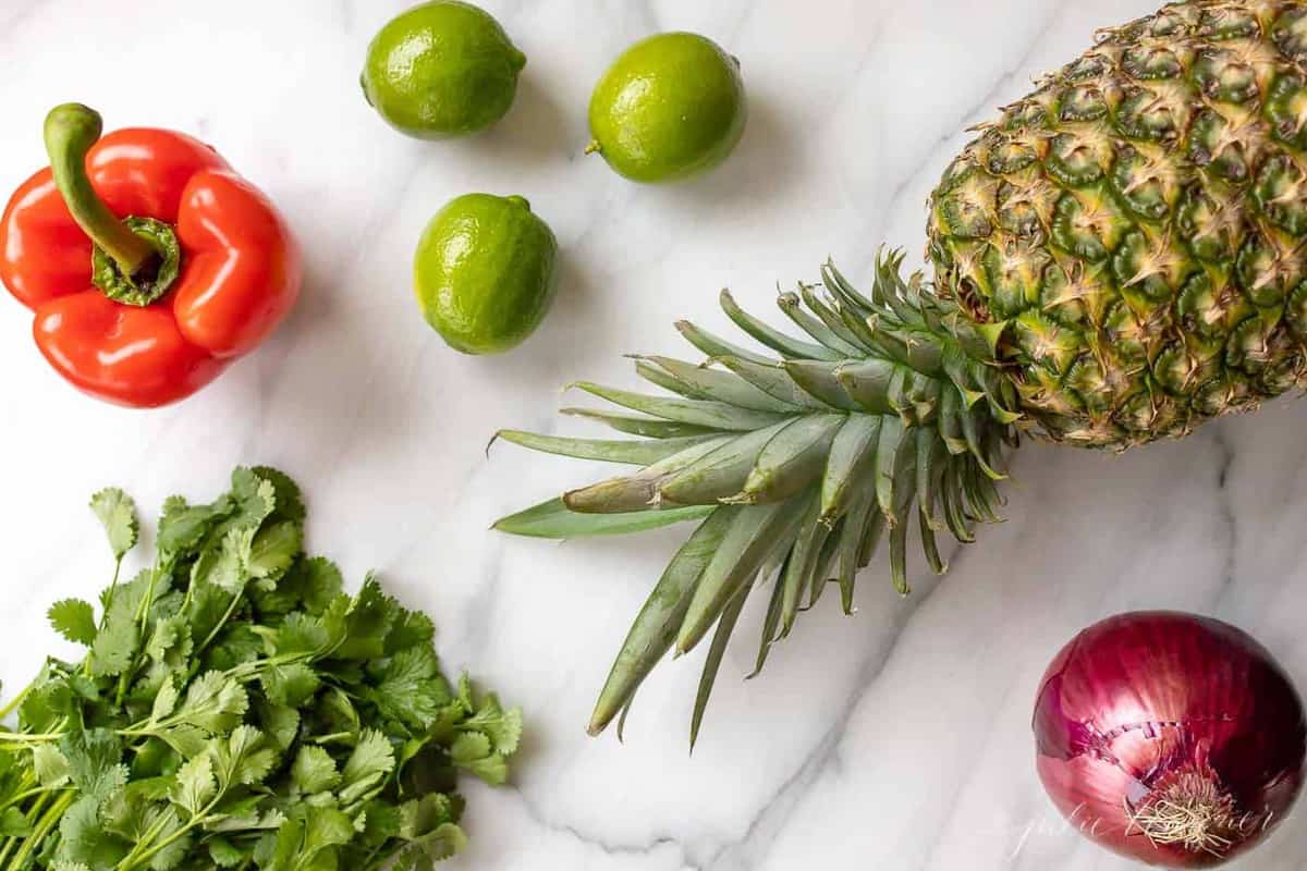 Marble surface with fruits and vegetables ready to make pineapple salsa.