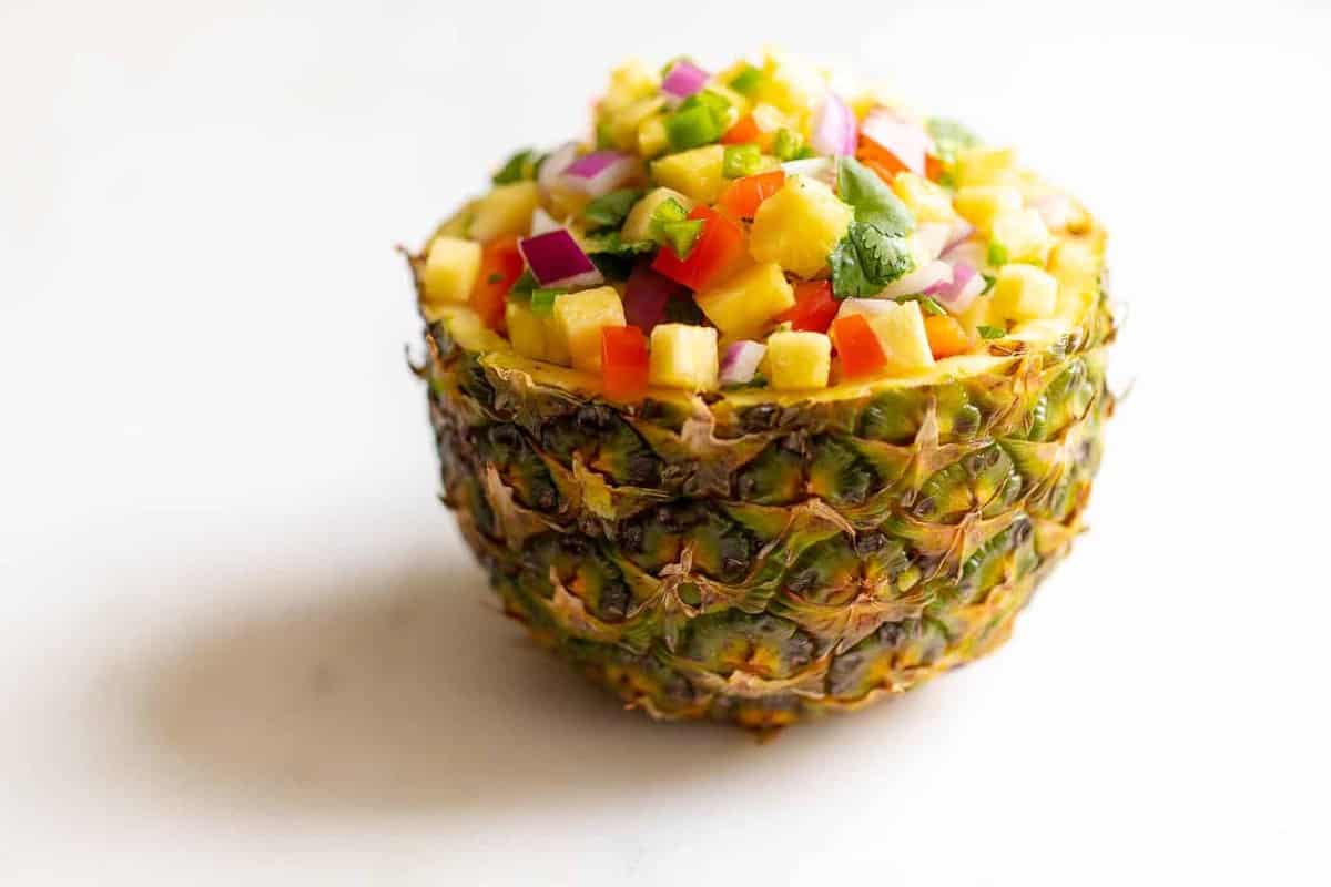 A fresh bowl made from a cut pineapple, filled with a pineapple salsa recipe.