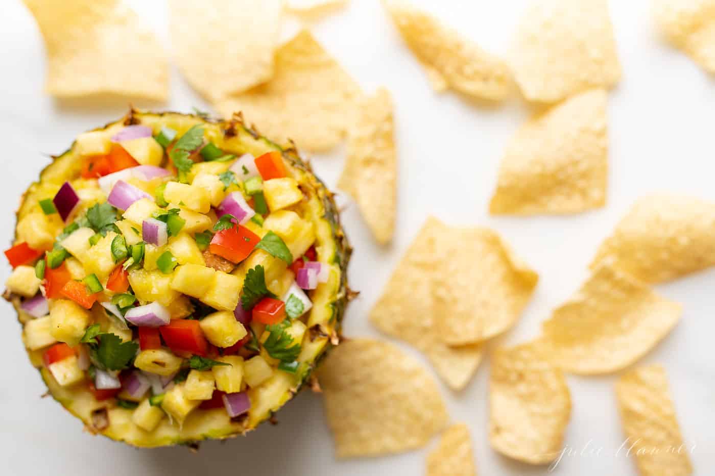 Corn salsa in a pineapple bowl, surrounded by tortilla chips.