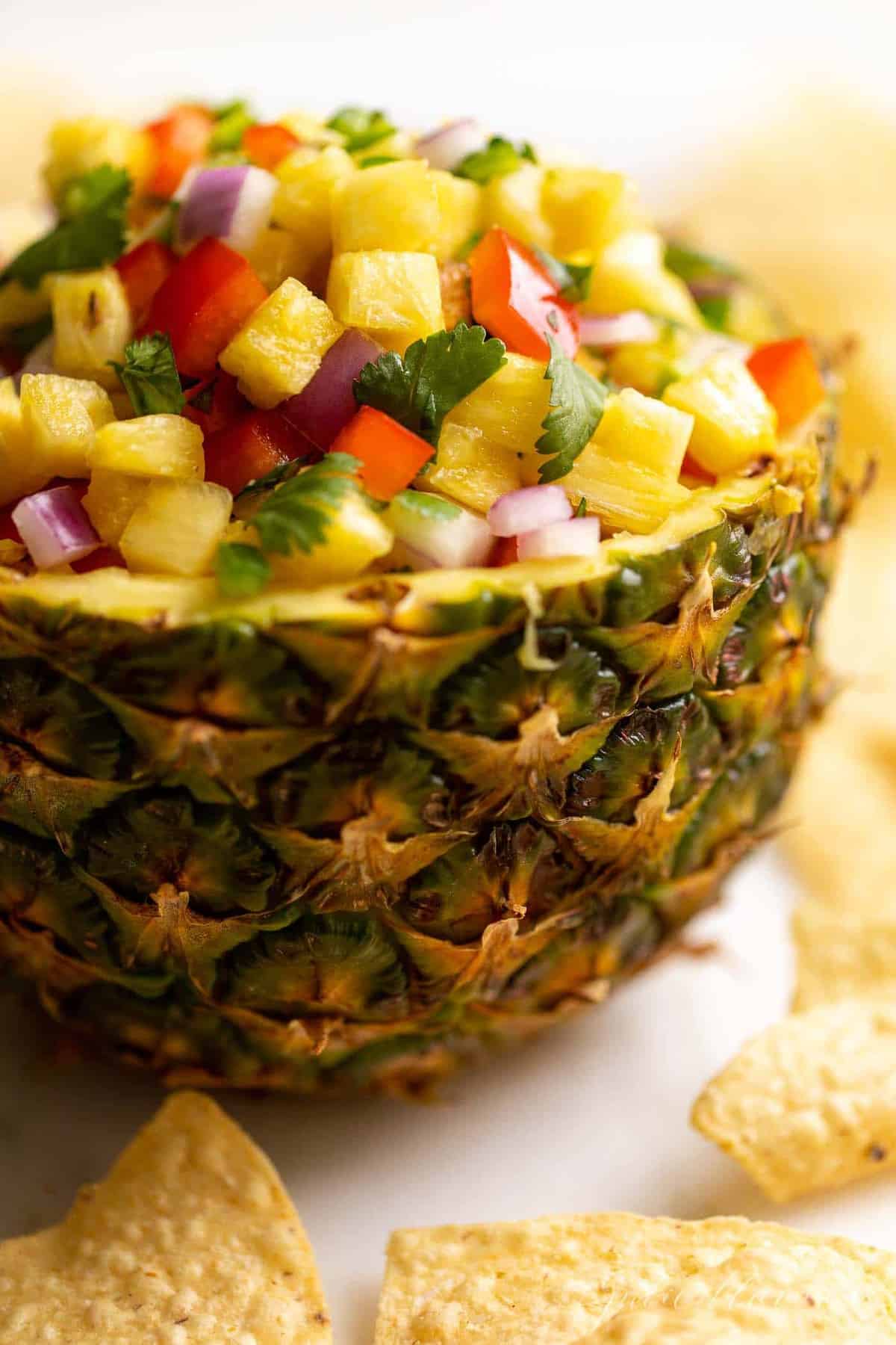 A fresh bowl made from a cut pineapple, filled with pineapple salsa.
