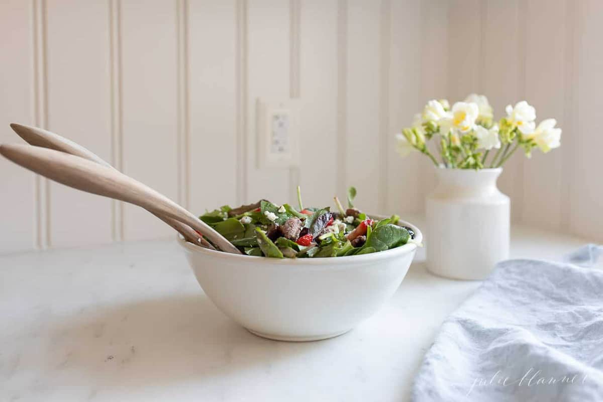 A white kitchen background, with a white bowl full of spring salad