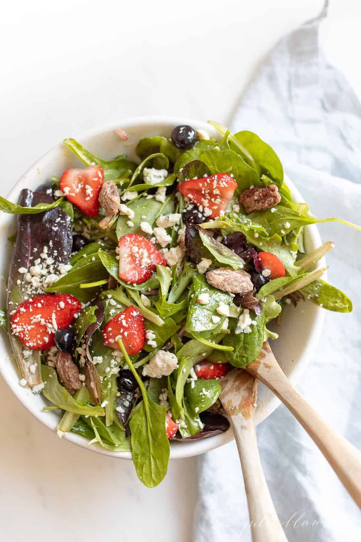 Spring salad in a glass bowl, a wooden spoon and linen napkin to the side. 