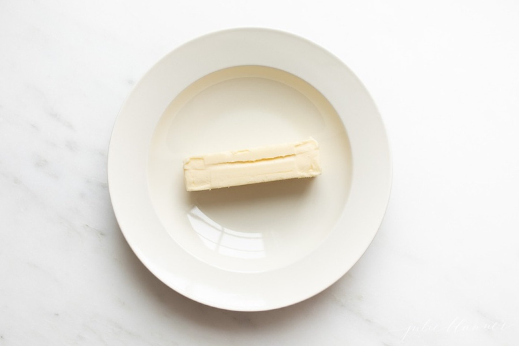 A single stick of butter on a white plate.