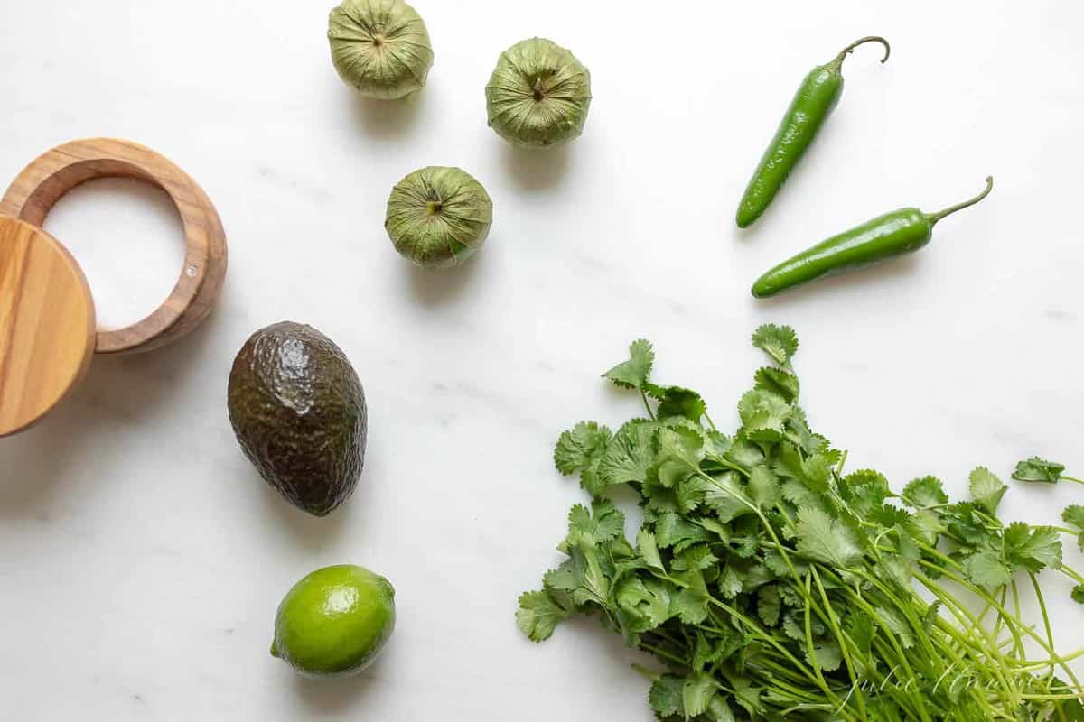 A marble surface covered in fresh ingredients to make guacamole salsa.