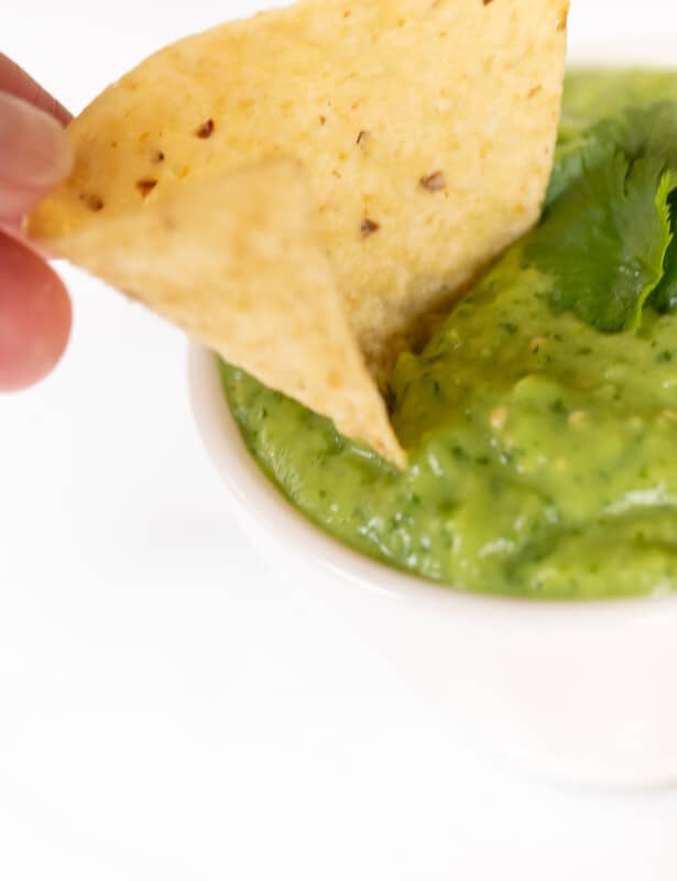 A bowl full of avocado salsa, hand reaching in with a chip for dipping.