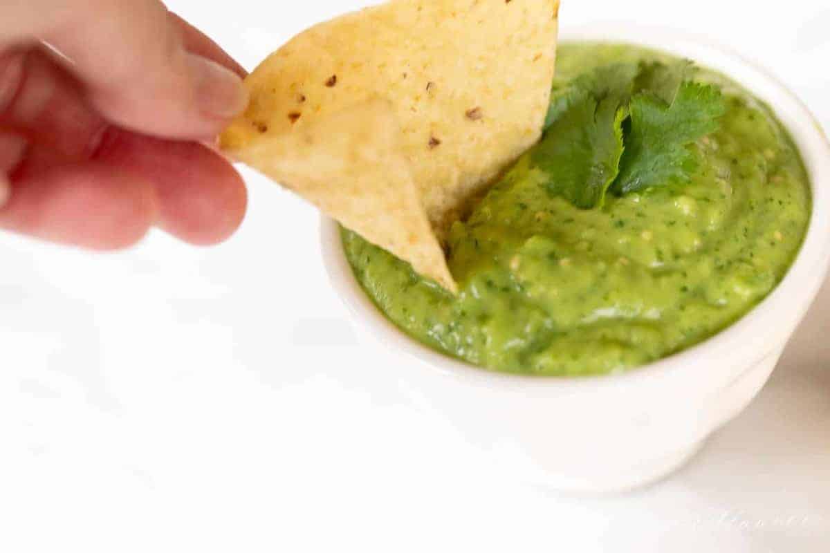 A bowl full of avocado salsa, hand reaching in with a chip for dipping.