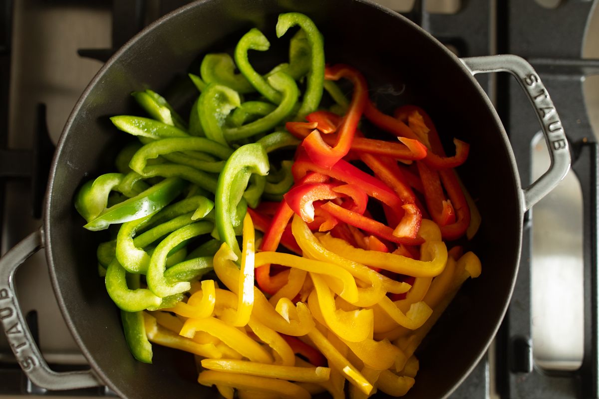 Fresh sliced colorful bell peppers in a cast iron sauté pan on a stovetop.