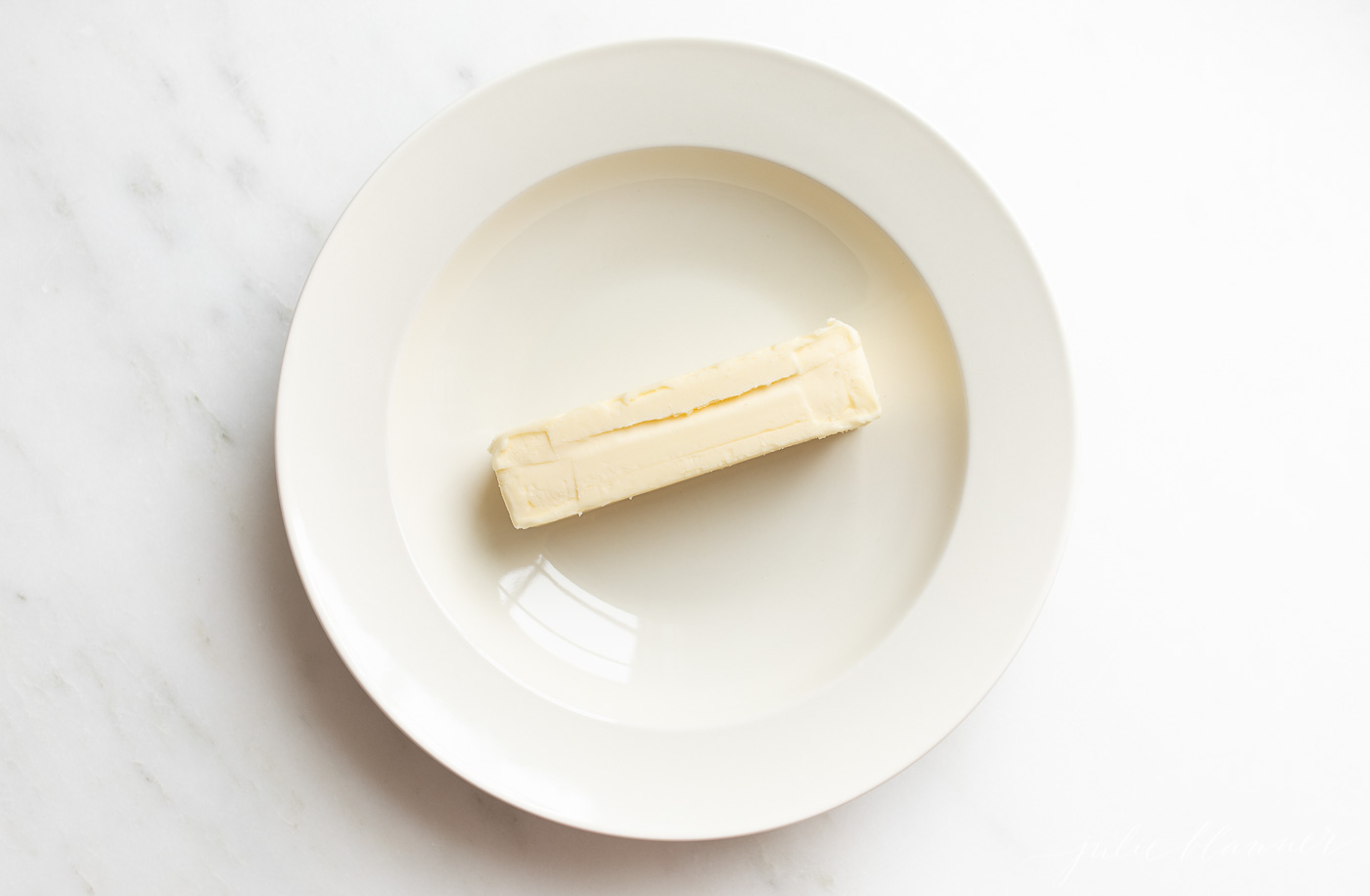 A white plate on a white surface, stick of butter in the center.