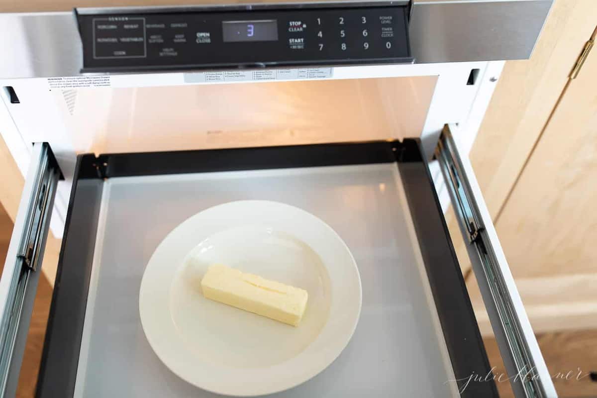 White plate with a stick of butter inside microwave.