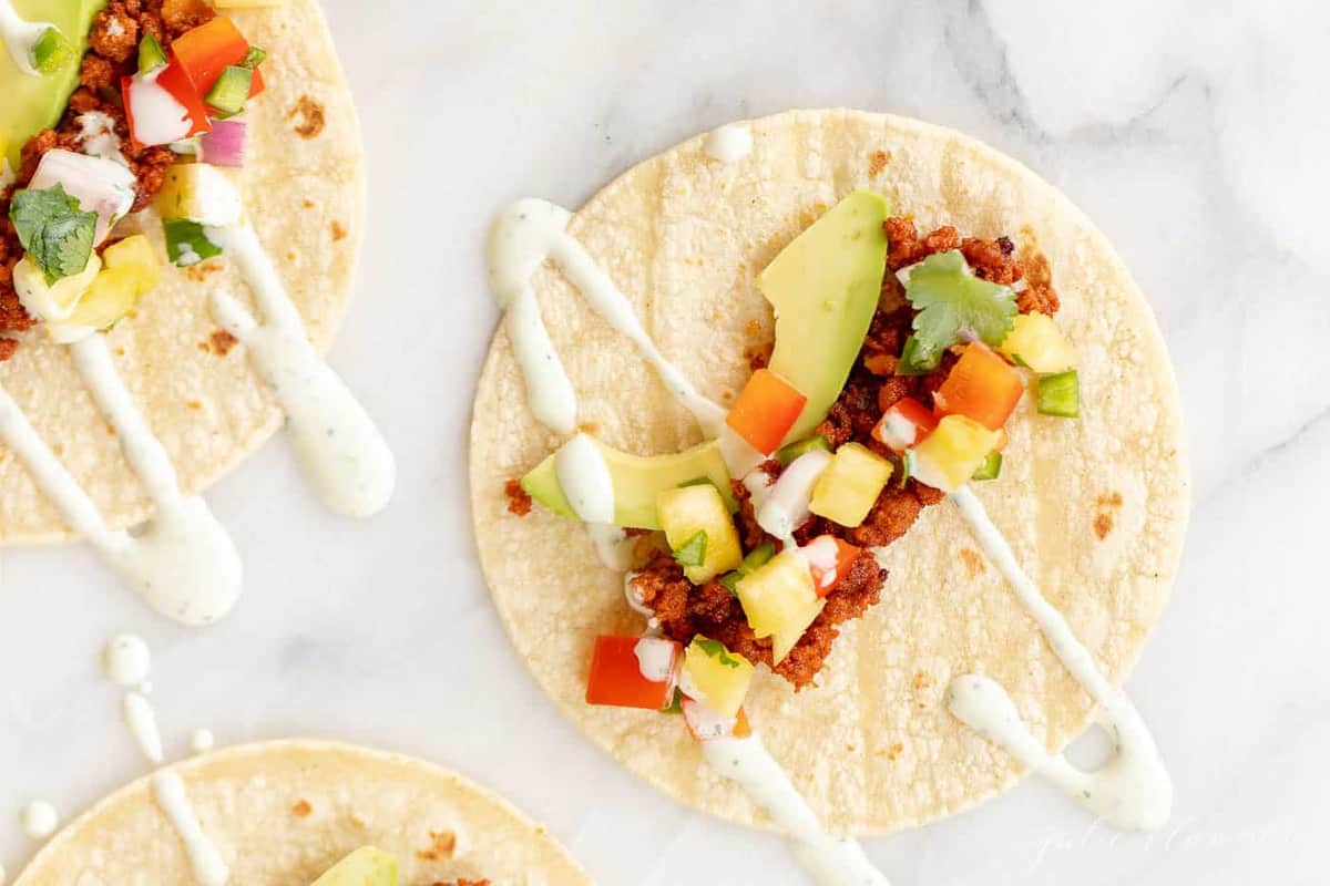 marble surface with three chorizo tacos loaded with toppings