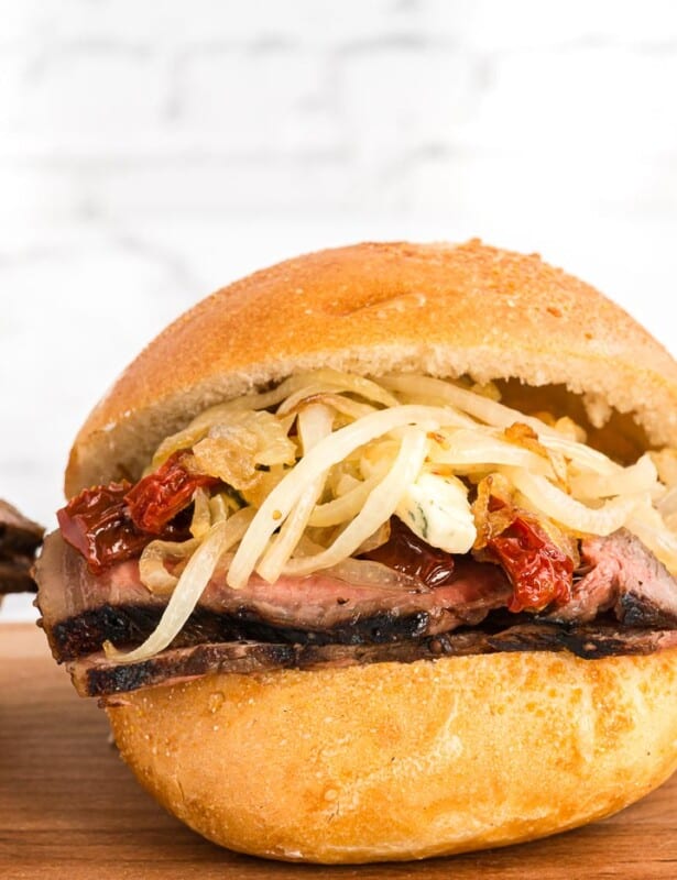 A trio of steak sandwiches stacked with ingredients on a round bun.