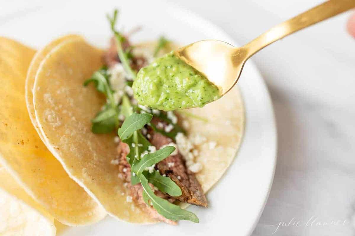 A steak taco with a gold spoon placing sauce on top