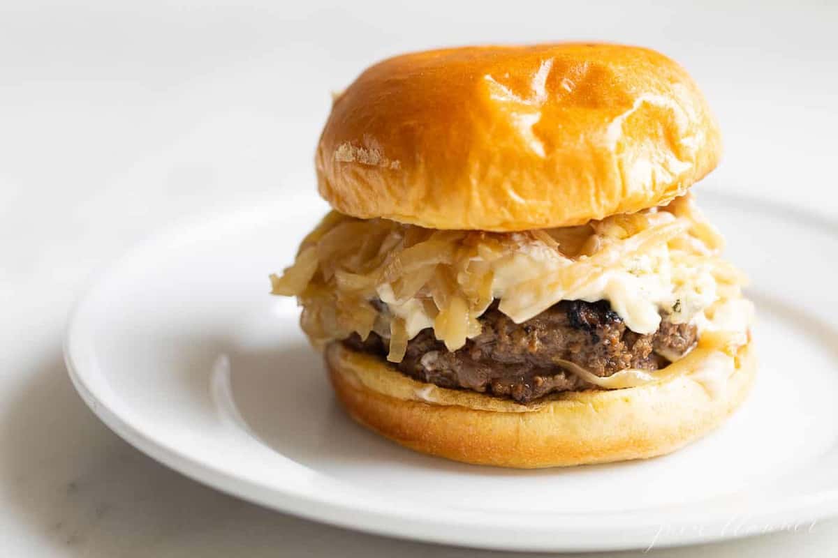 A gourmet burger on a white plate with a white background. 