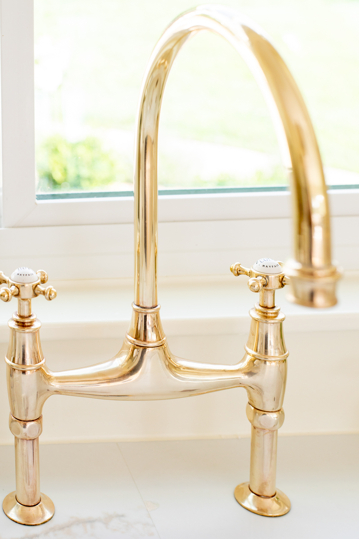An unlacquered brass kitchen faucet in a white kitchen.