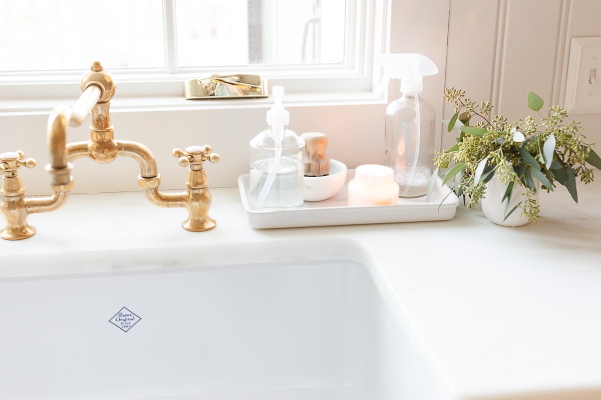 A white farmhouse sink with an unlacquered brass faucet.