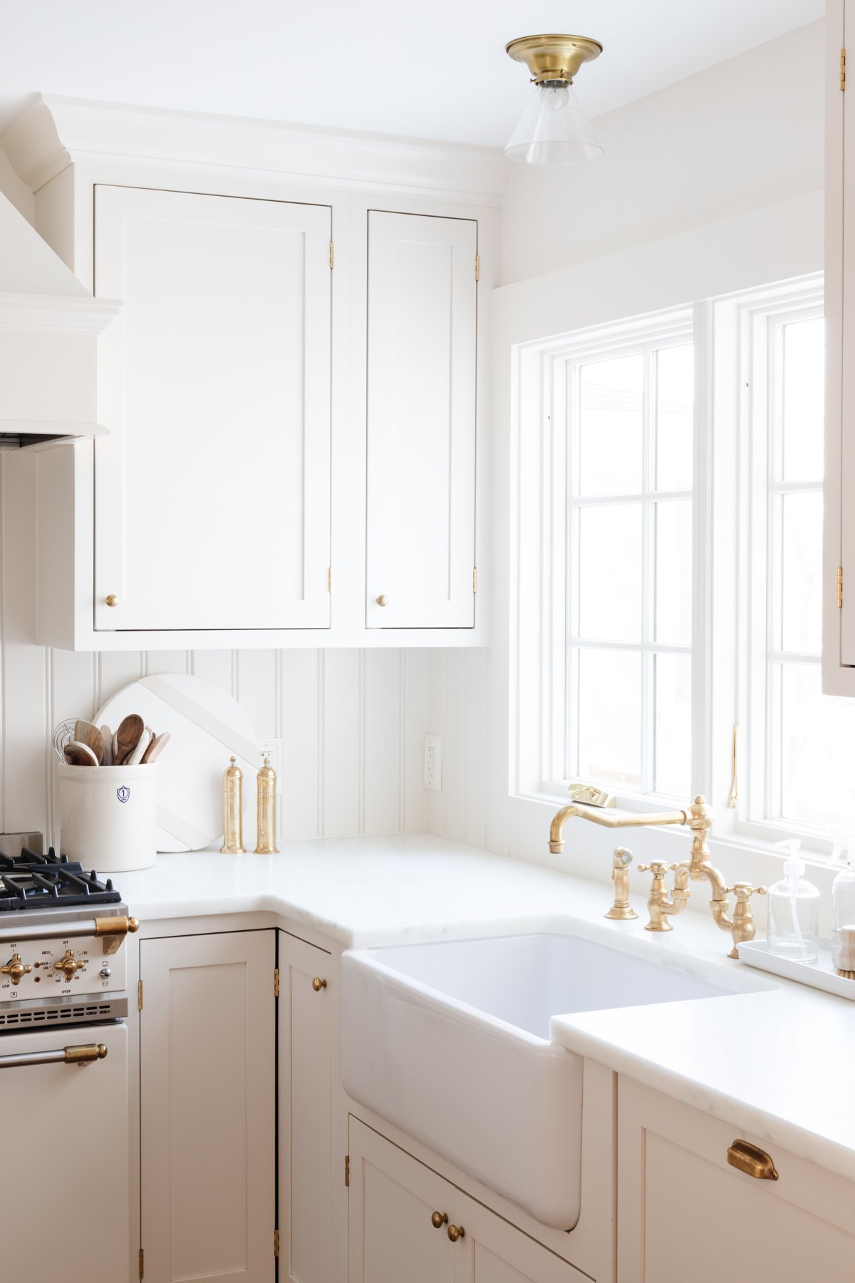 A white kitchen with a farmhouse sink and an unlacquered brass faucet.
