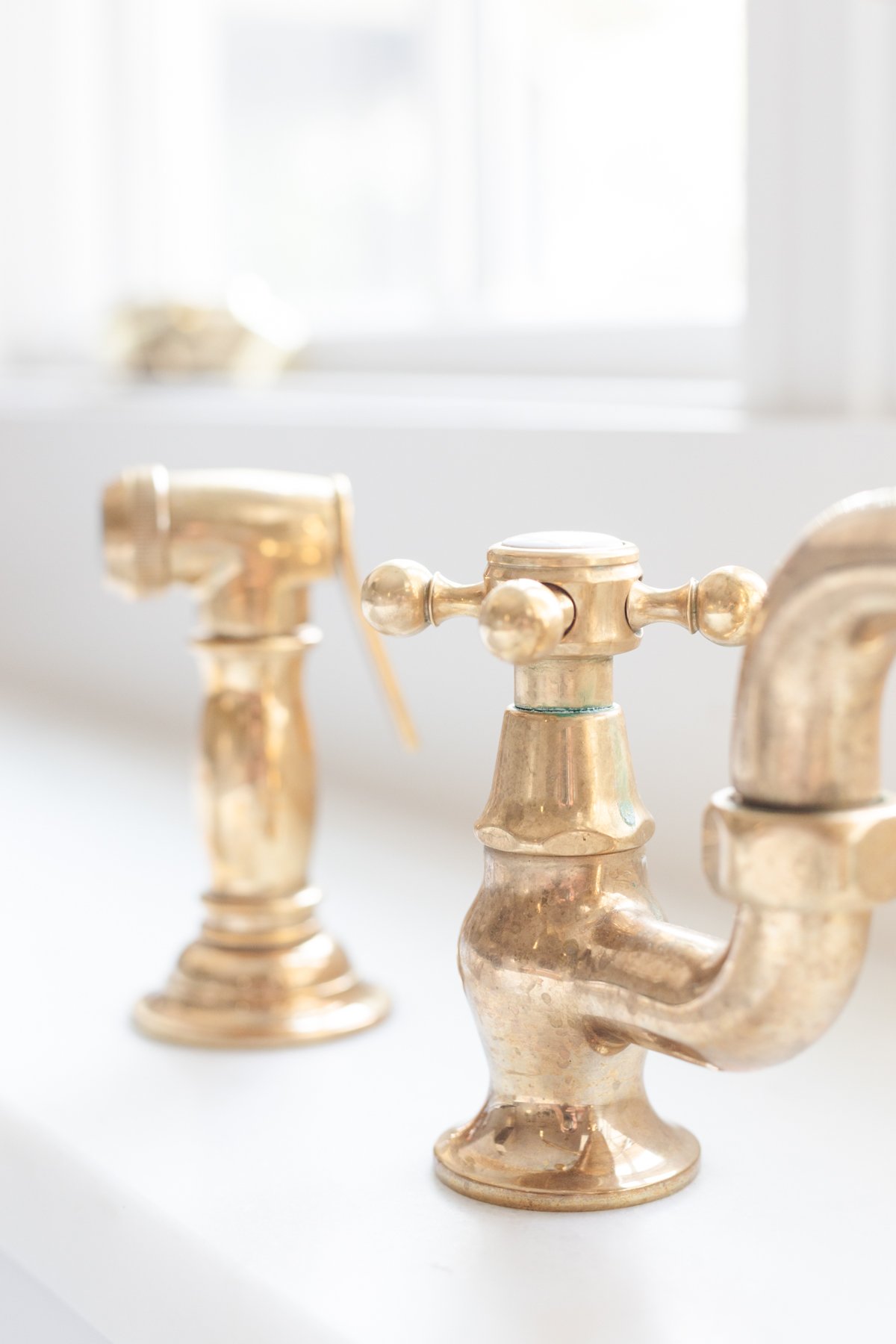 A white farmhouse sink with an unlacquered brass faucet.