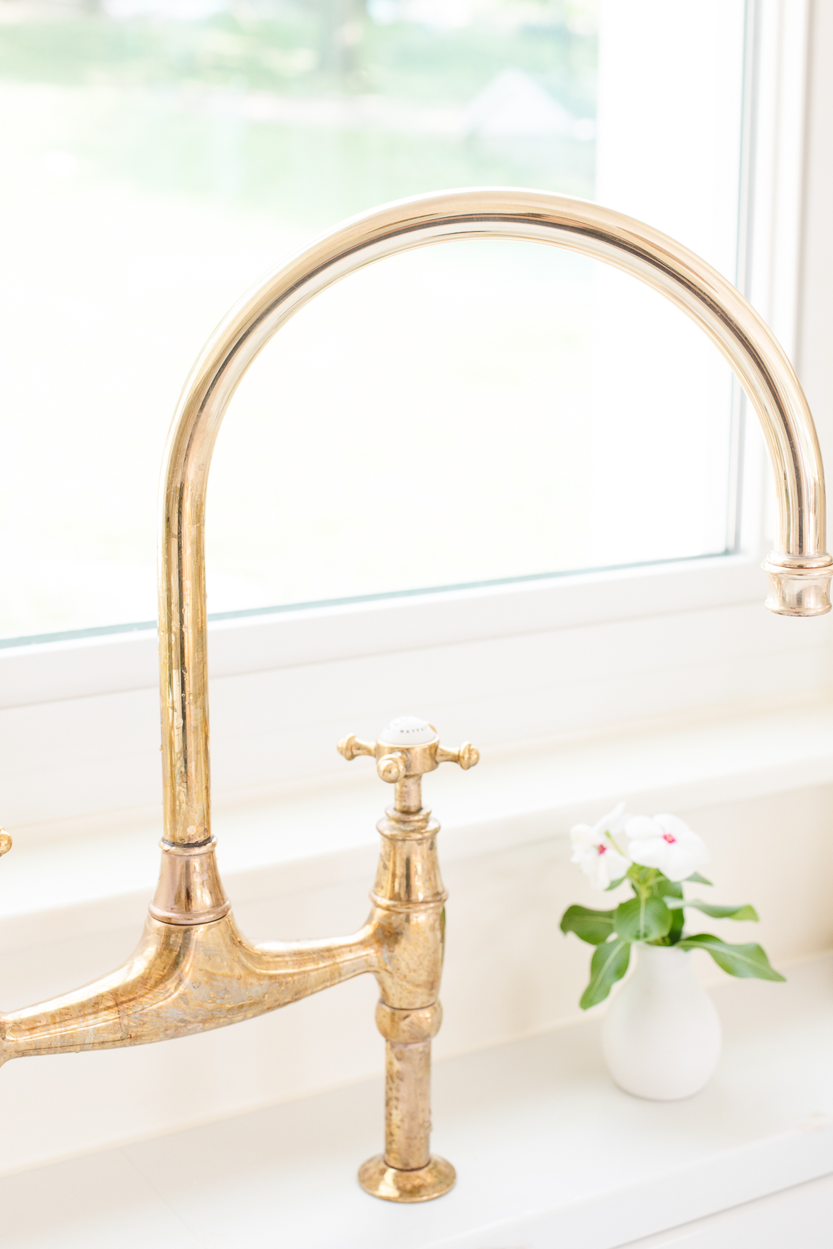 An unlacquered brass kitchen faucet in a white kitchen.