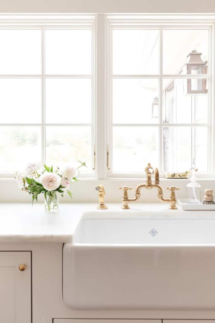 A kitchen sink with a brass faucet and a white peony flower arrangement to the side.