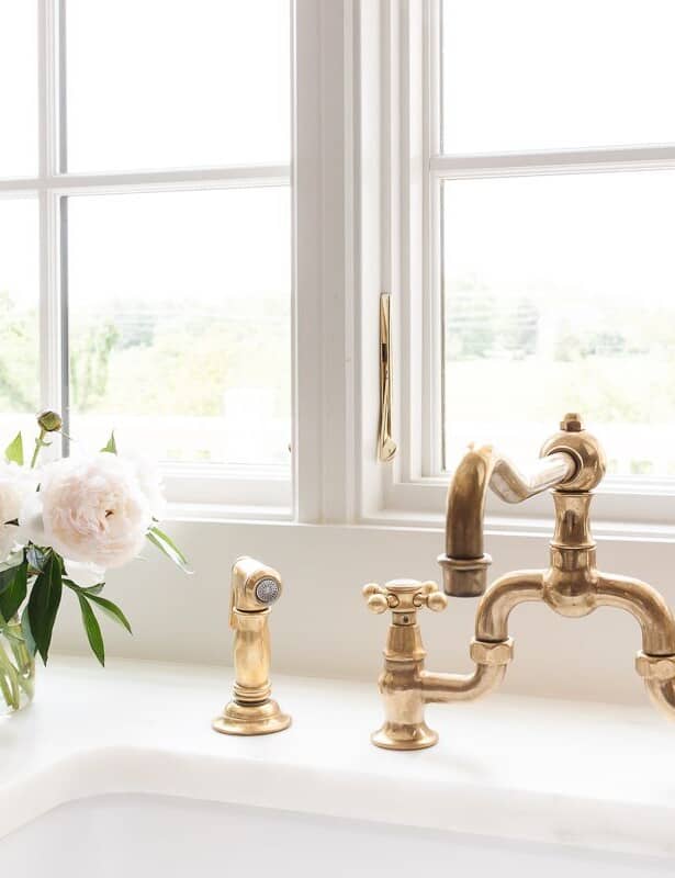 A kitchen sink with a brass faucet and a white peony flower arrangement to the side.