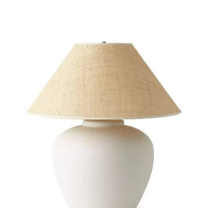 A white ceramic table lamp with an off-white fabric lampshade against a plain white background.