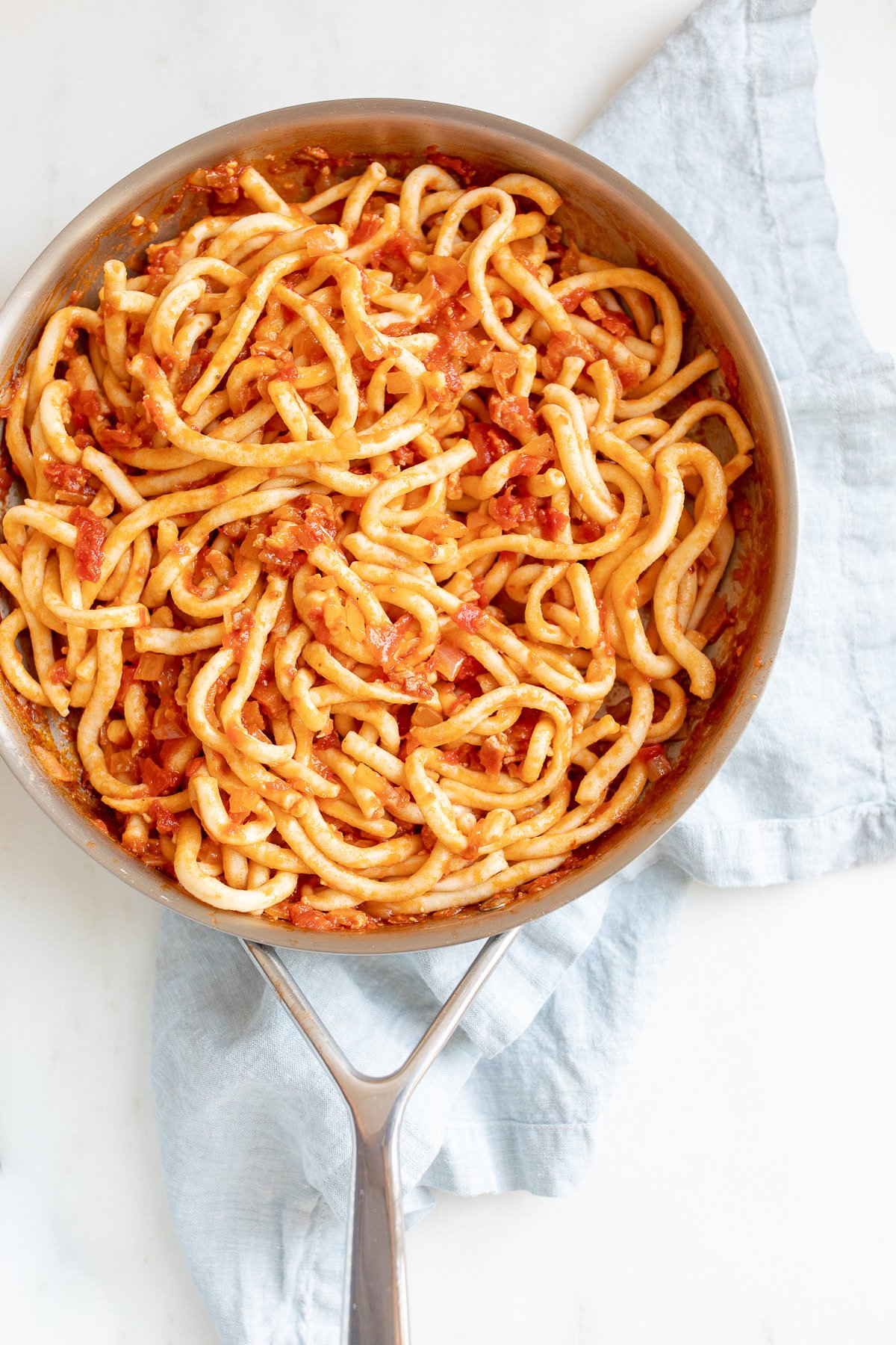 A skillet with amatriciana sauce-coated bucatini pasta.