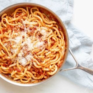 A silver pan, filled with Amatriciana pasta, topped with parmesan