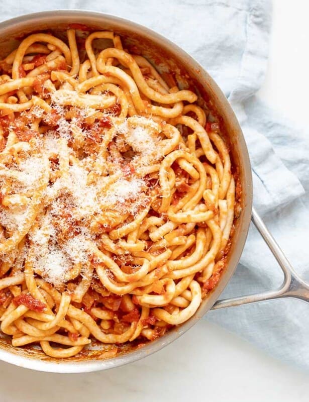 A silver pan, filled with Amatriciana pasta, topped with parmesan