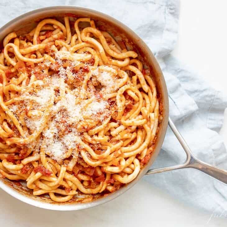 A silver pan, filled with Amatriciana pasta, topped with parmesan