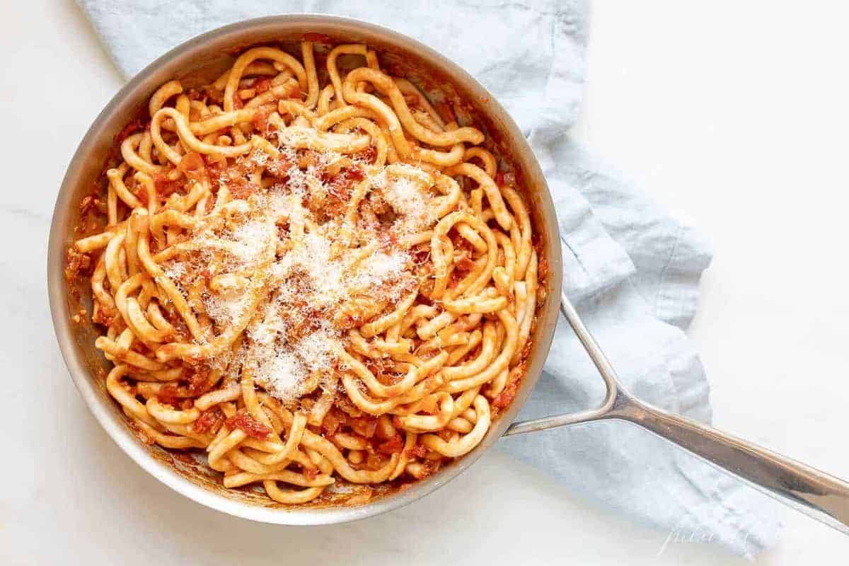A silver pan, filled with Amatriciana pasta, topped with parmesan