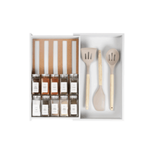 An organized kitchen drawer with labeled spice jars on the left and three beige cooking utensils on the right, neatly separated by drawer dividers.