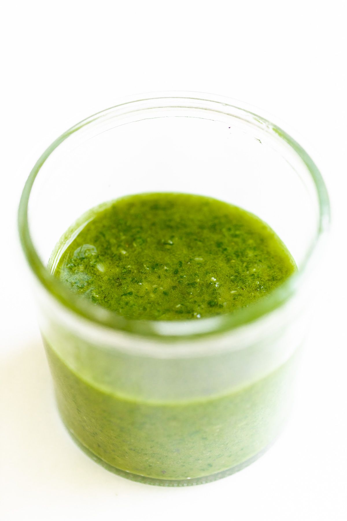 Basil pesto in a small clear glass jar on a marble surface.