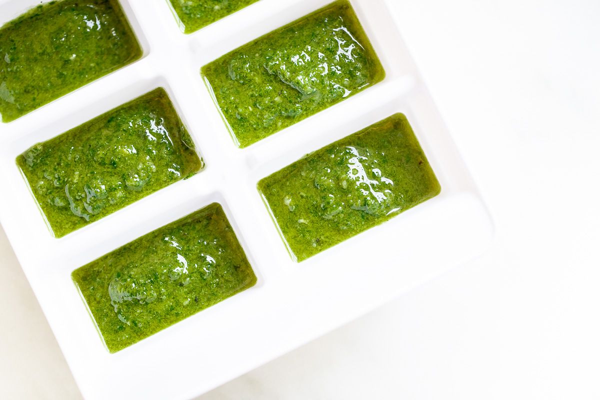 A white ice cube tray filled with basil pesto in each cube, for freezing