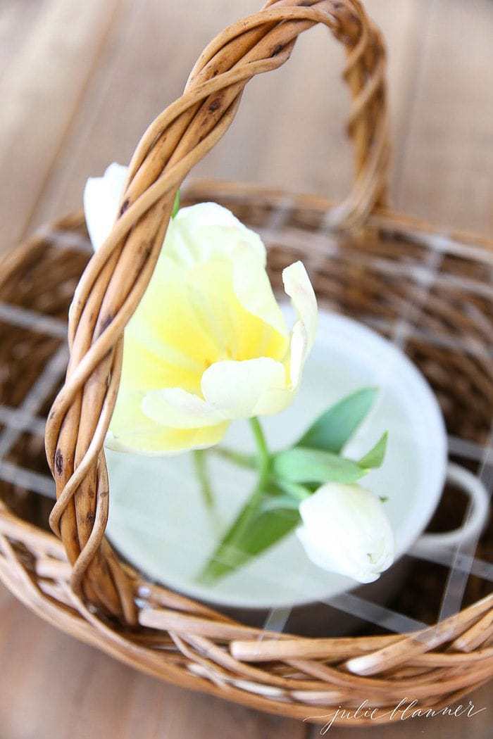 A wicker basket with a white dish inside, yellow tulips placed at the beginning of a flower basket arrangement.
