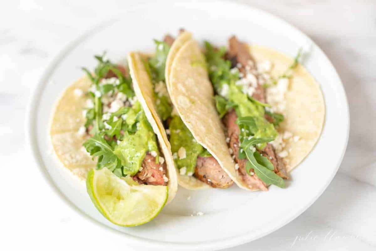A white plate filled with three carne asada tacos.