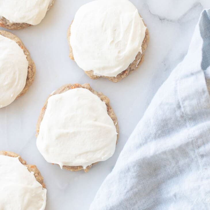 Frosted carrot cake cookies on a marble surface, blue linen towel to the side.