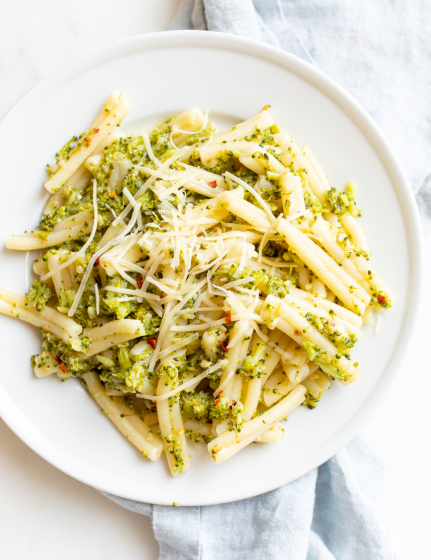 A white plate filled with broccoli pasta, blue napkin behind.
