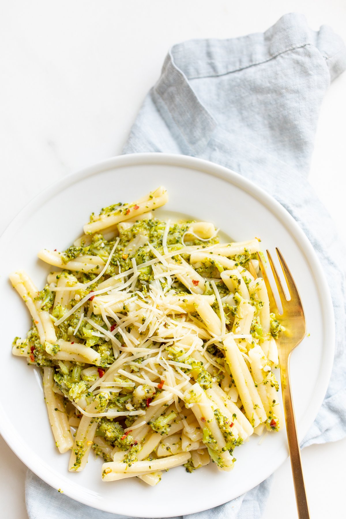 A white plate filled with broccoli pasta, blue napkin behind.