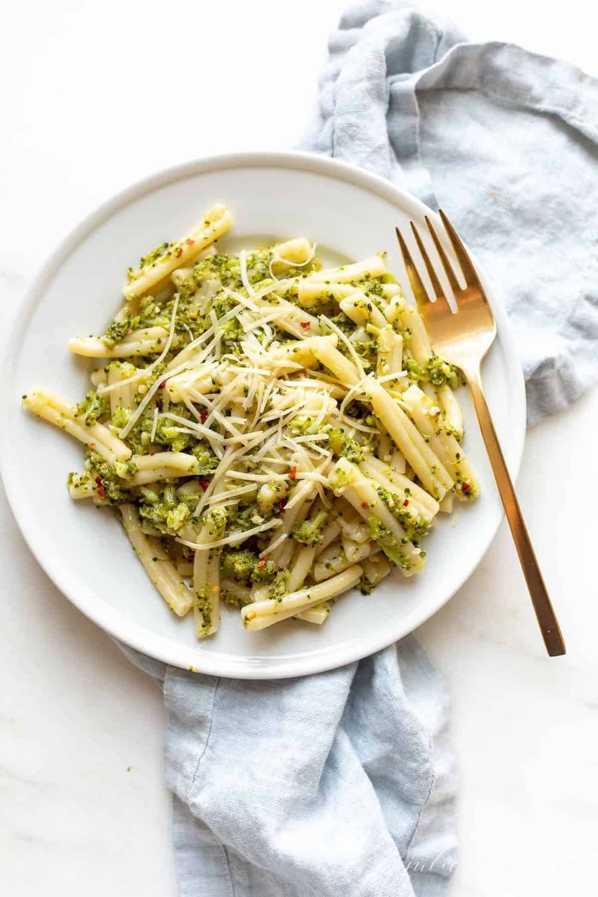 A white plate filled with broccoli sauce and pasta, gold fork to the side