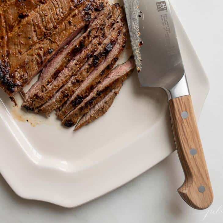 White platter with sliced carne asada, knife to the side