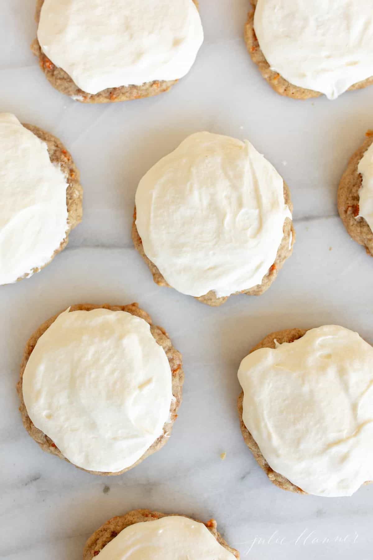 Carrot cake cookies frosted with cream cheese frosting on a marble surface.