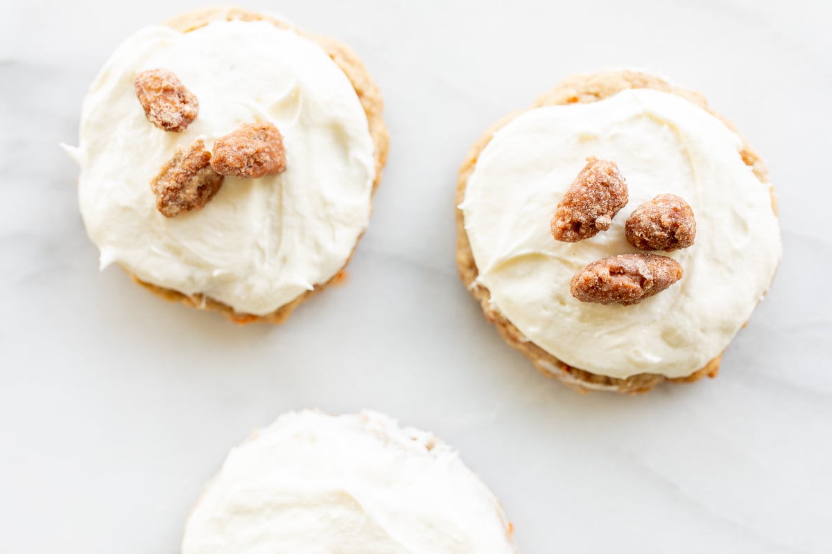 Carrot cake cookies topped with cream cheese frosting and candied pecans on top.