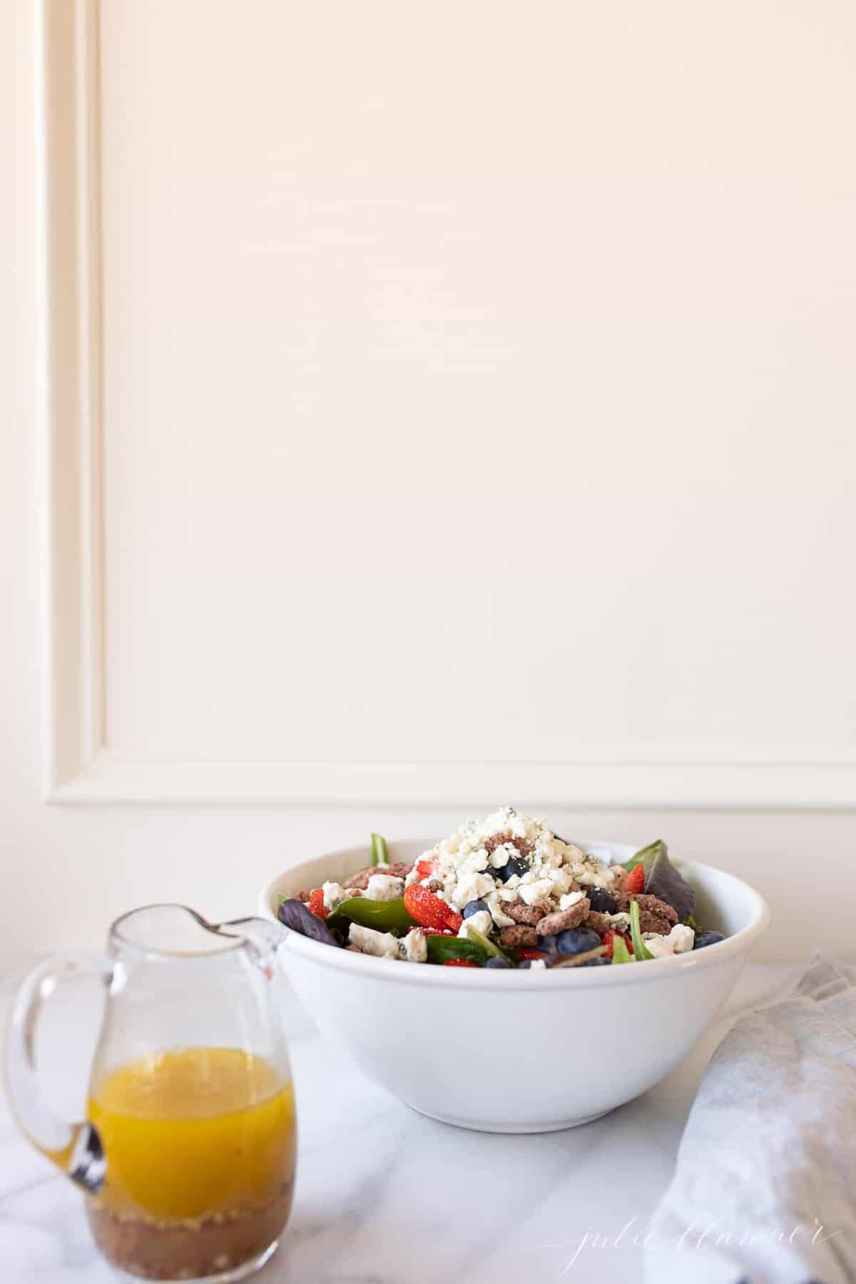 Vinaigrette in a glass pitcher on a marble surface, with a summer salad to the side.