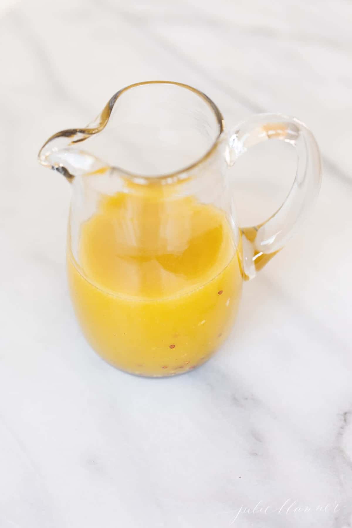 Vinaigrette in a glass pitcher on a marble surface.