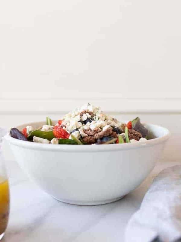 A white kitchen background with a white bowl full of salad and champagne vinaigrette in a clear pitcher.
