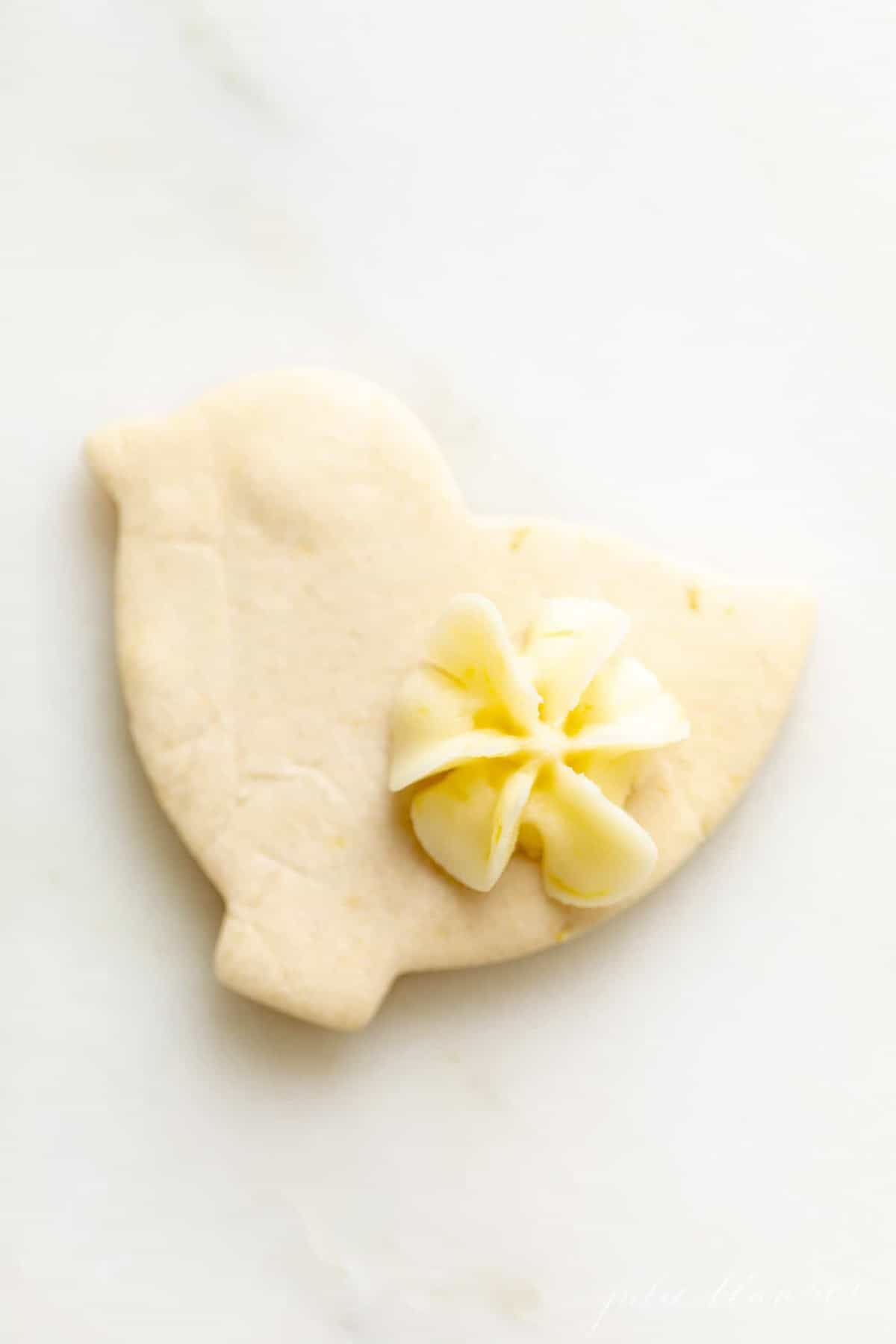 A duck shaped cookies, frosted with lemon icing in the shape of a small flower.