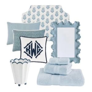 A set of blue and white home decor items, including pillows, a monogrammed cushion, a scalloped wastebasket, a decorative mirror, and neatly folded towels.